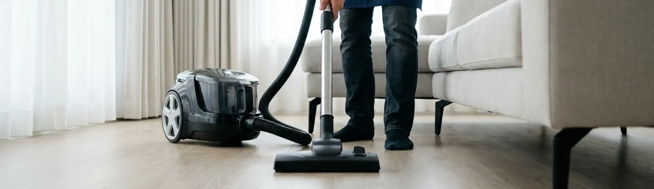 Professional house cleaner vacuuming a living room floor with a canister vacuum cleaner, Fargo, ND.