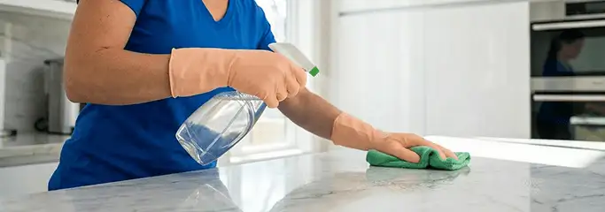 Maid service worker spraying and wiping a kitchen countertop with a microfiber cloth for sanitizing, Fargo, ND.