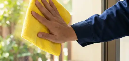 House cleaner wiping a glass window with a yellow microfiber cloth for streak-free cleaning, Fargo, ND.